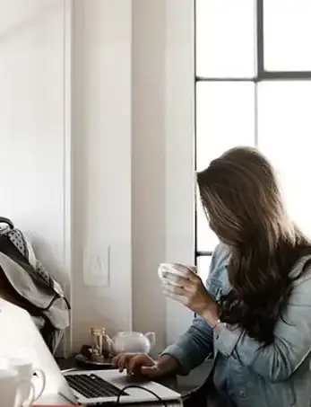 Online therapy woman on laptop holding a cup of coffee while talking to a therapist